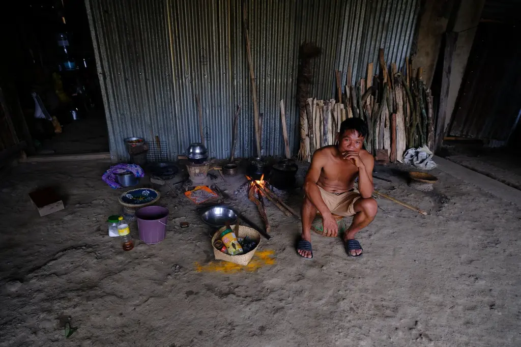 A single cooking-gas cylinder stands against the wall of a camp room; on the floor beside it a blackened pot sits over a small heap of firewood, the way the cooking is done once the gas runs out.
