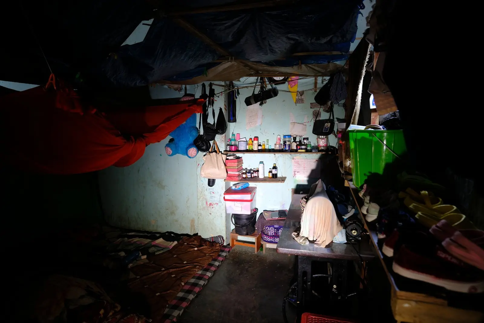 A narrow wooden shelf against a bare camp wall holds a sparse, half-empty row of medicine bottles and foil strips — most of the slots are bare.